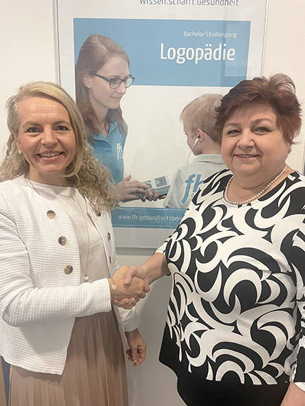 Zwei Personen stehen vor einem Plakat der FHG OÖ mit dem Titel Logopädie. Links ist eine Frau mit hellem, gelockten über die Schulter gehenden langen Haar, helle Kleidung, sie schüttelt der neben ihr stehenden Frau die Hand. Diese hat kurzes, dunkles Haar und trägt ein schwarz, weiß gemustertes Oberteil. Zwei Personen stehen vor einem Plakat der FHG OÖ mit dem Titel Logopädie. Links ist eine Frau mit hellem, gelockten über die Schulter gehenden langen Haar, helle Kleidung, sie schüttelt der neben ihr stehenden Frau die Hand. Diese hat kurzes, dunkles Haar und trägt ein schwarz, weiß gemustertes Oberteil.