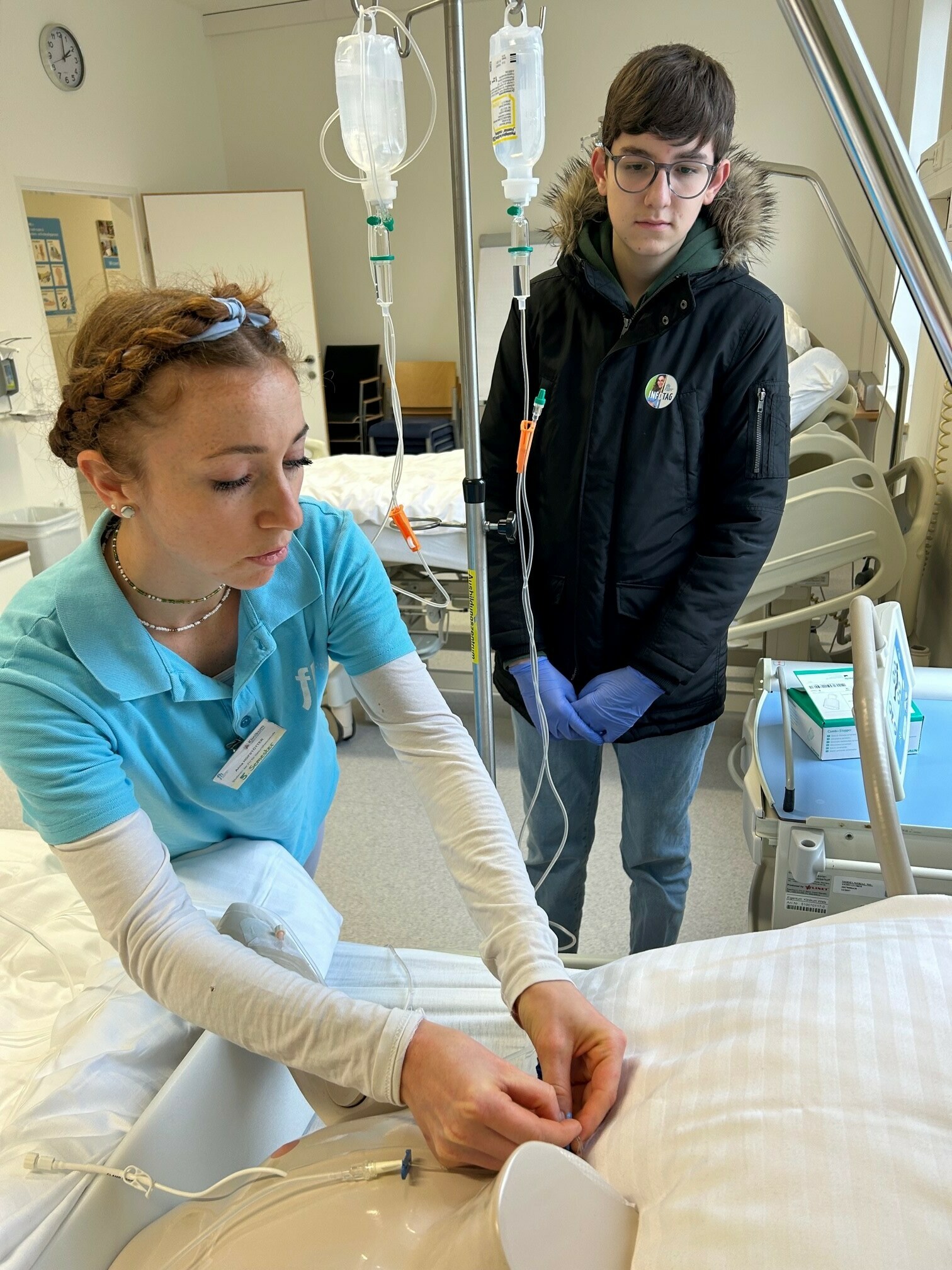 Eine Studierende zeigt einem Interessenten etwas am Krankenbett  (vergrößerete Ansicht in der Galerie)
