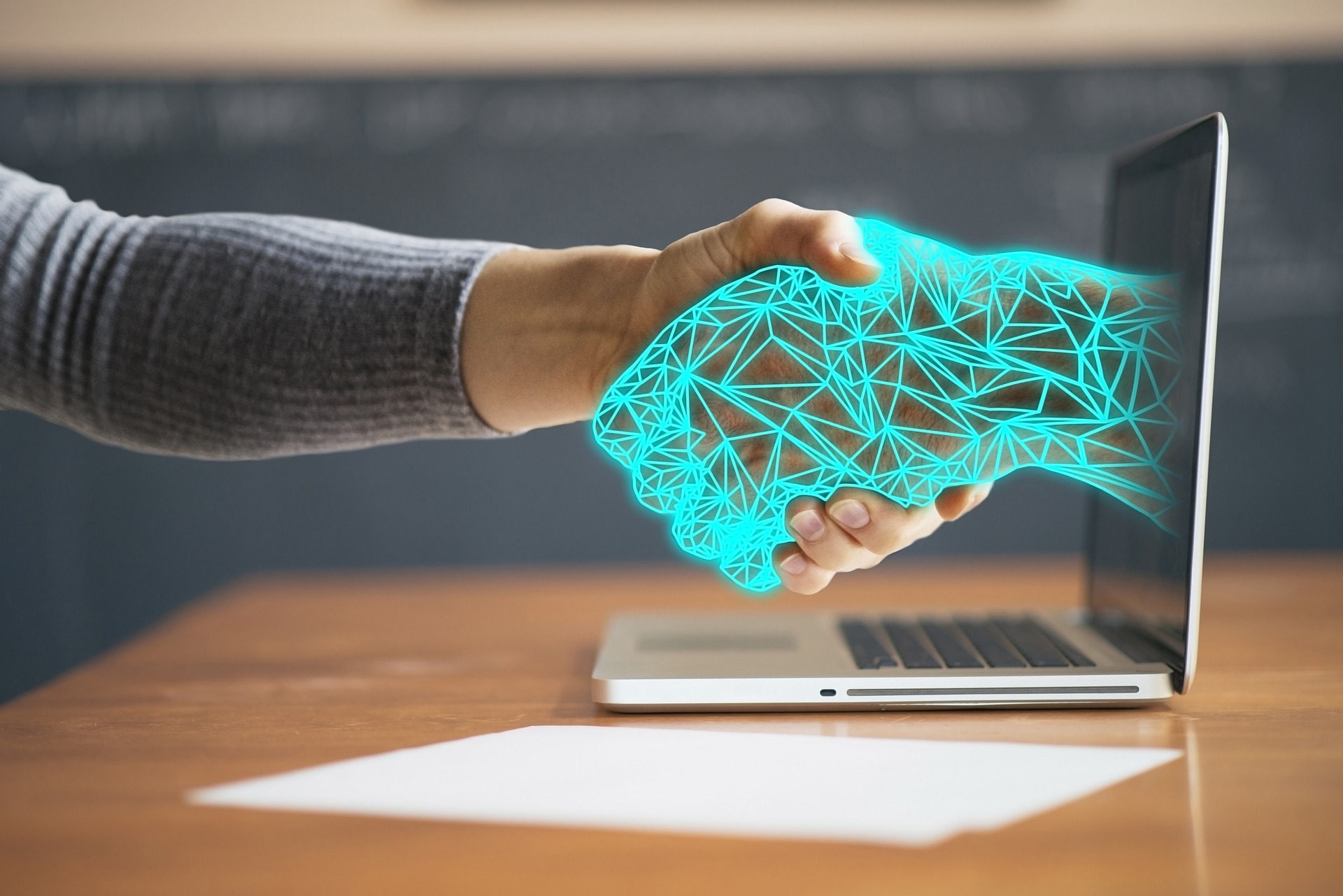 Das Bild zeigt einen Handschlag zwischen einer realen Hand und einer stilisierten Hand, die aus einem Computerbildschirm herausragt. 